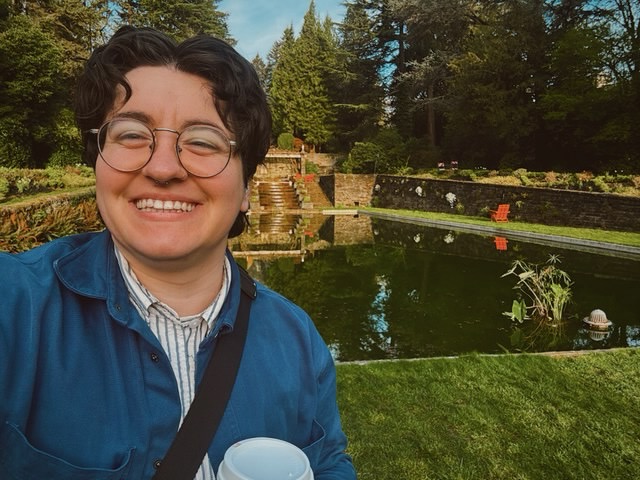 Rowan Ono of Stages Planning Group, smiling and standing in a grassy park near a reflecting pool