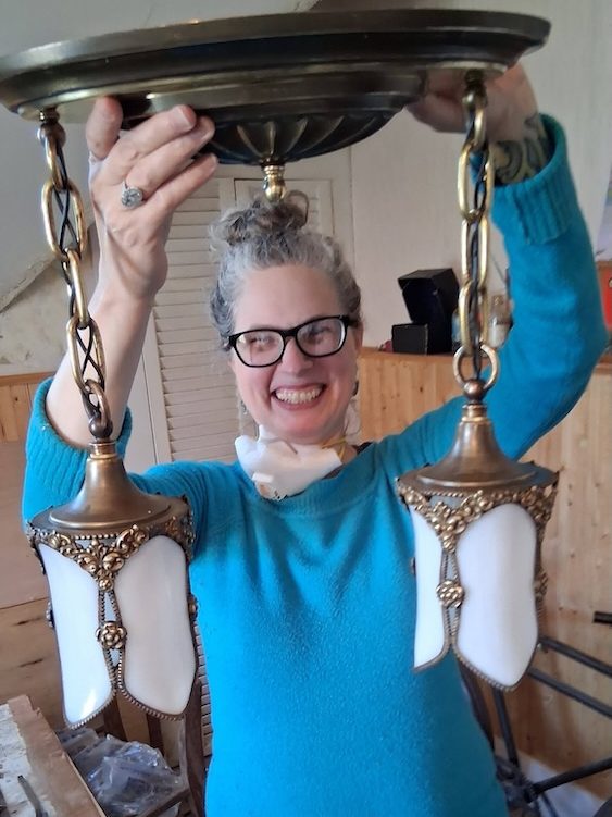 Tanisha Caravello of Stages Planning Group, smiling and holding up a vintage chandelier